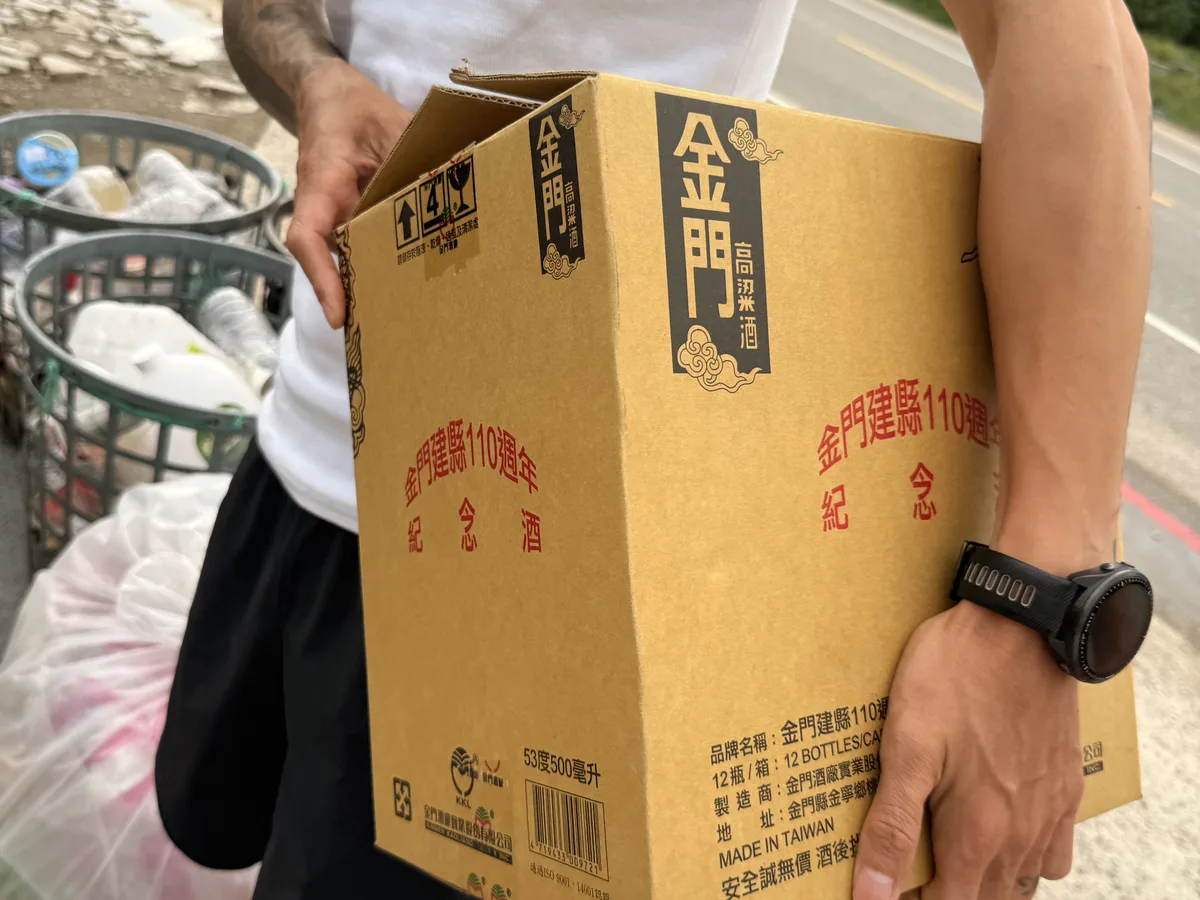 一個人抱著整箱金門高粱酒的紙箱走在路邊